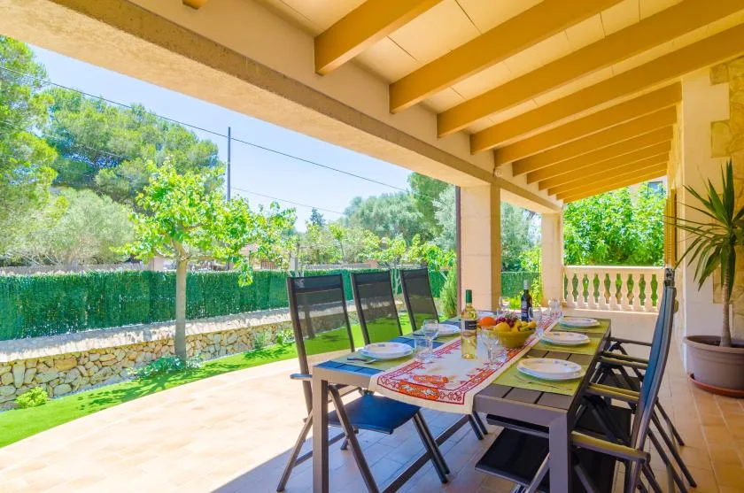 A covered outdoor dining area with a long table overlooking a green garden.