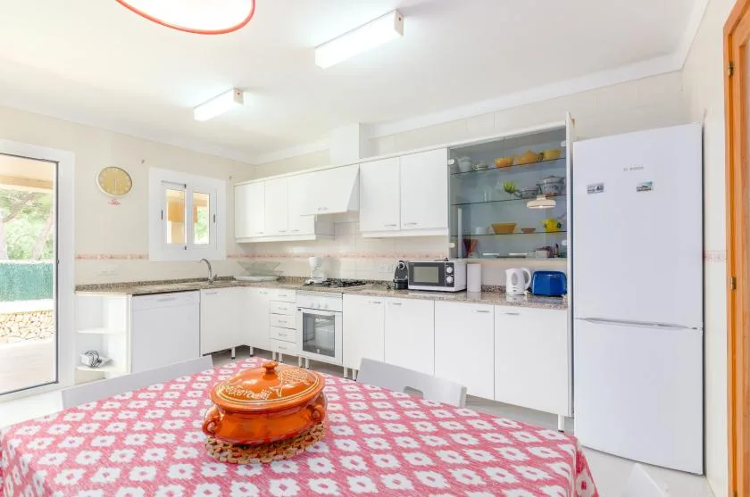 A bright kitchen with white cabinets and a patterned tablecloth in the foreground.