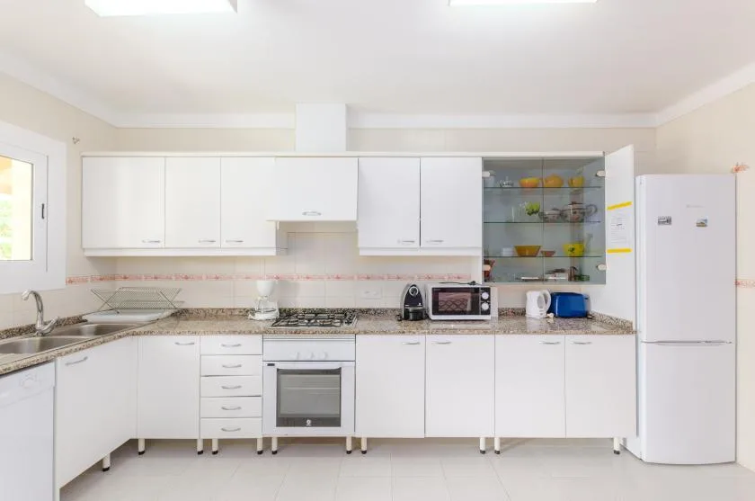 A bright kitchen with white cabinets, a countertop, and a refrigerator.
