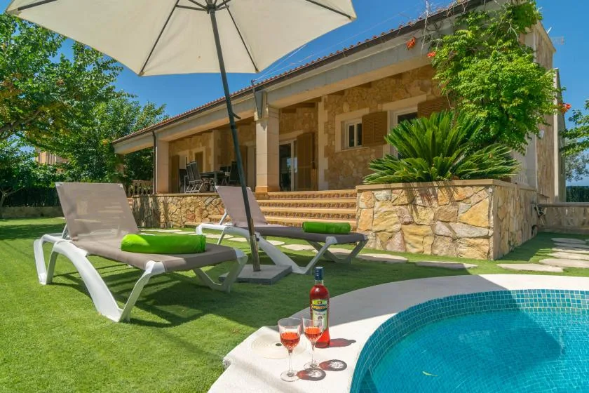 A sunny garden patio with loungers, an umbrella, and a small swimming pool.