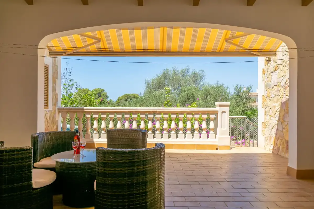 A covered terrace with wicker seating overlooks a garden and trees.