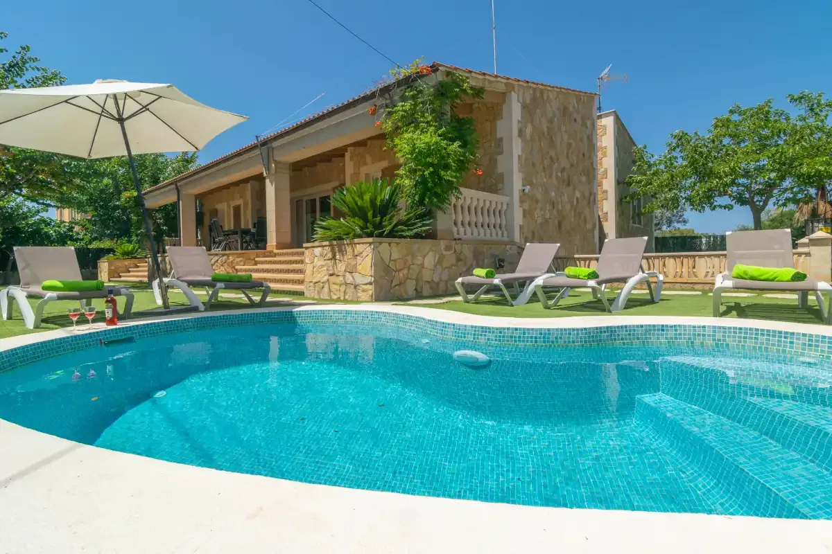 An outdoor swimming pool sits beside a house and patio seating.