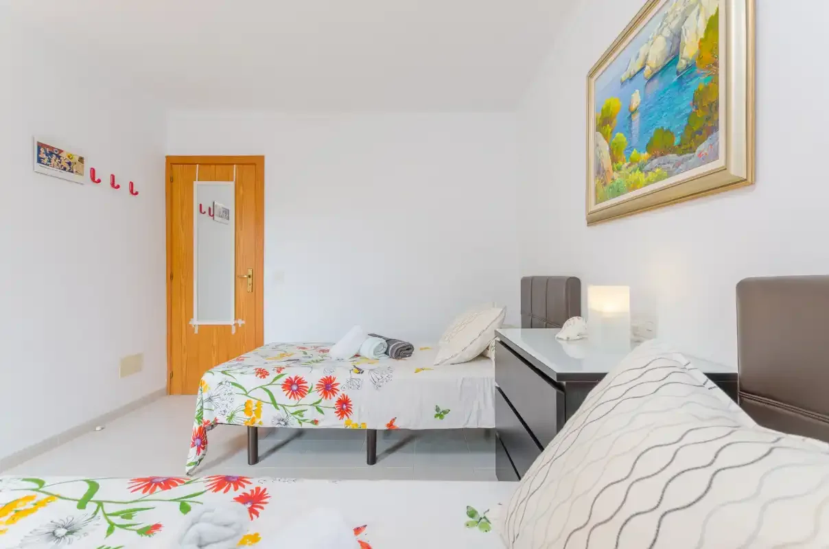 A bedroom with beds, a desk, and a colorful painting on the wall.