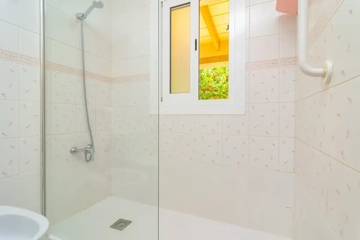 A tiled bathroom with a shower and a small window.