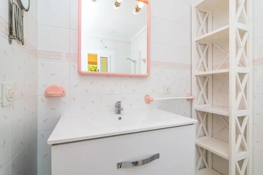A bright bathroom with a sink vanity, mirror, and open shelving.