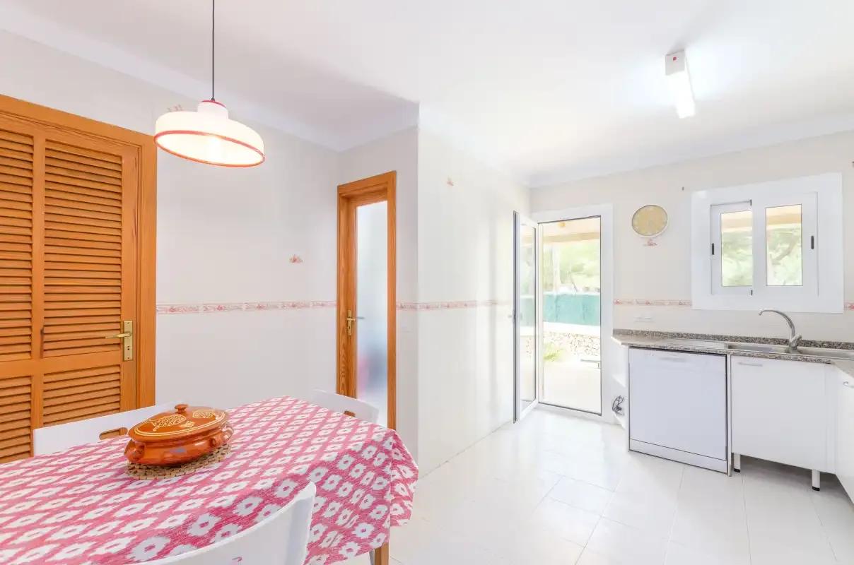 A bright kitchen and dining area with a patterned tablecloth and white cabinetry.