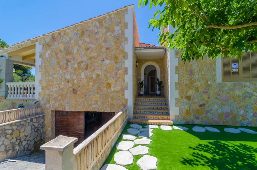 A stone-faced house entrance opens onto a lawn with a stepping-stone path.