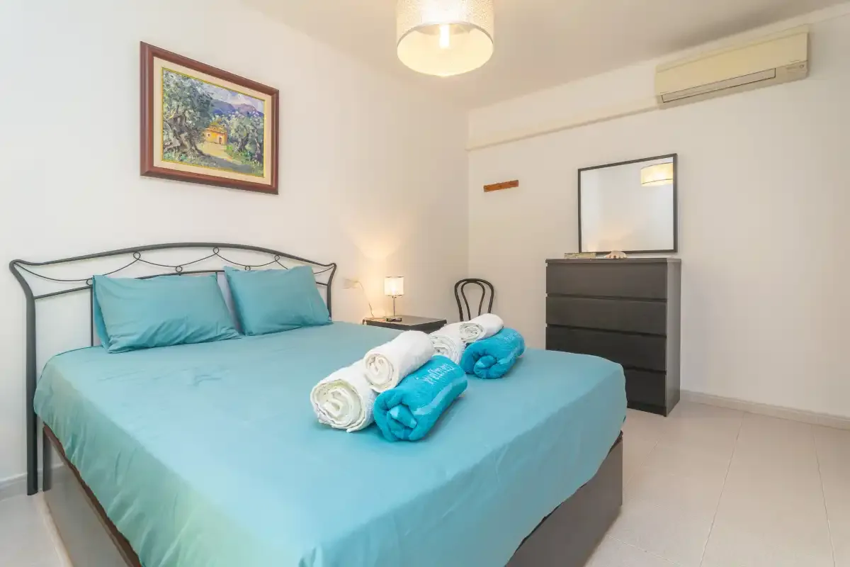 A bedroom with a turquoise bed, folded towels, and a dresser.