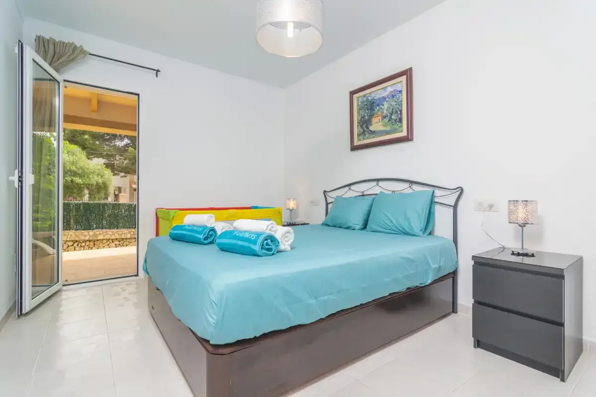 A bedroom with a bed covered in turquoise bedding and an open balcony door.