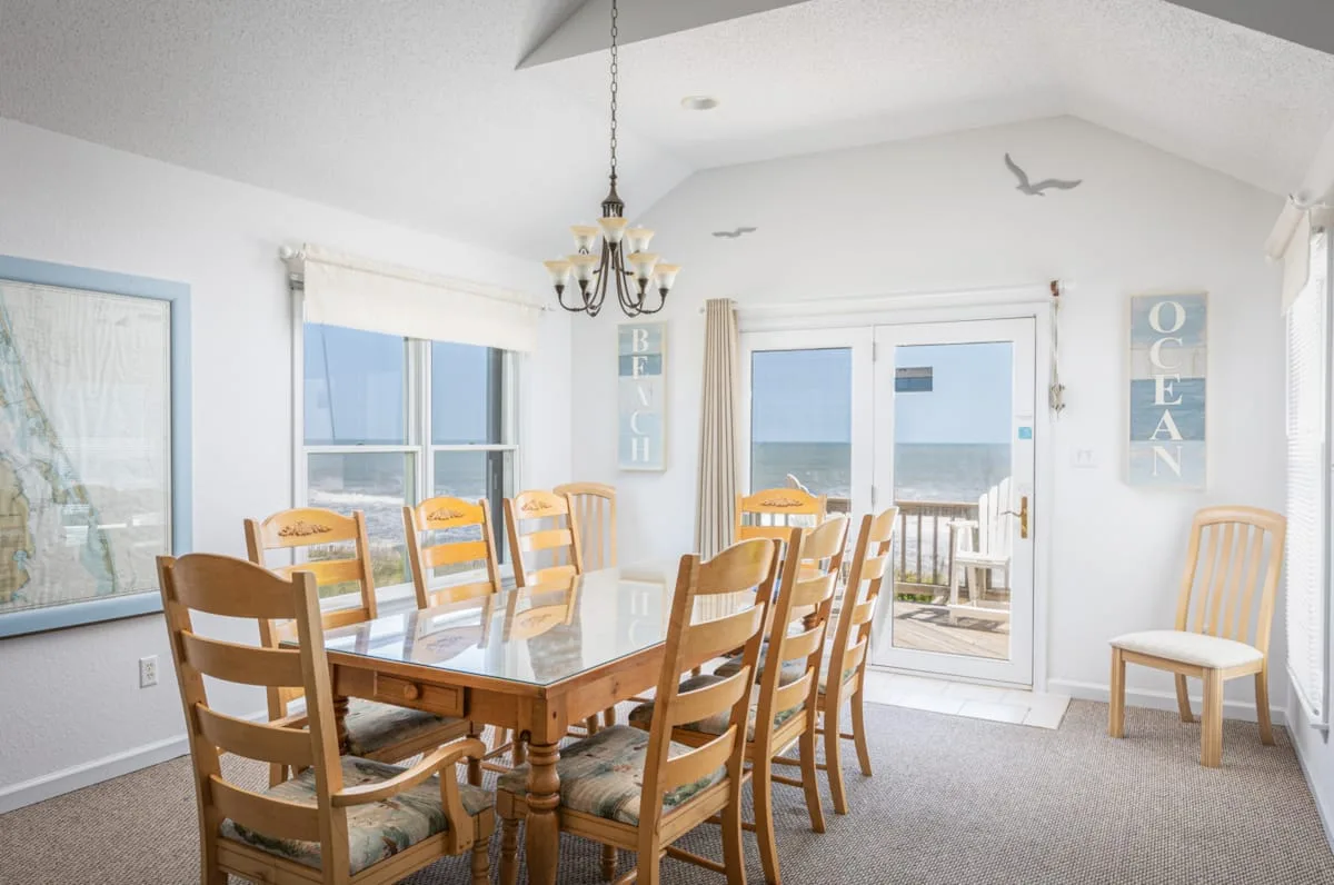 Un comedor luminoso con una mesa de madera y ventanas con vistas al agua.