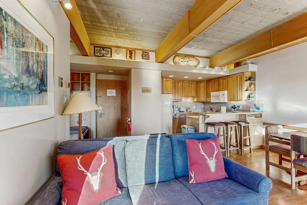 A living room with blue seating and a kitchen in the background.