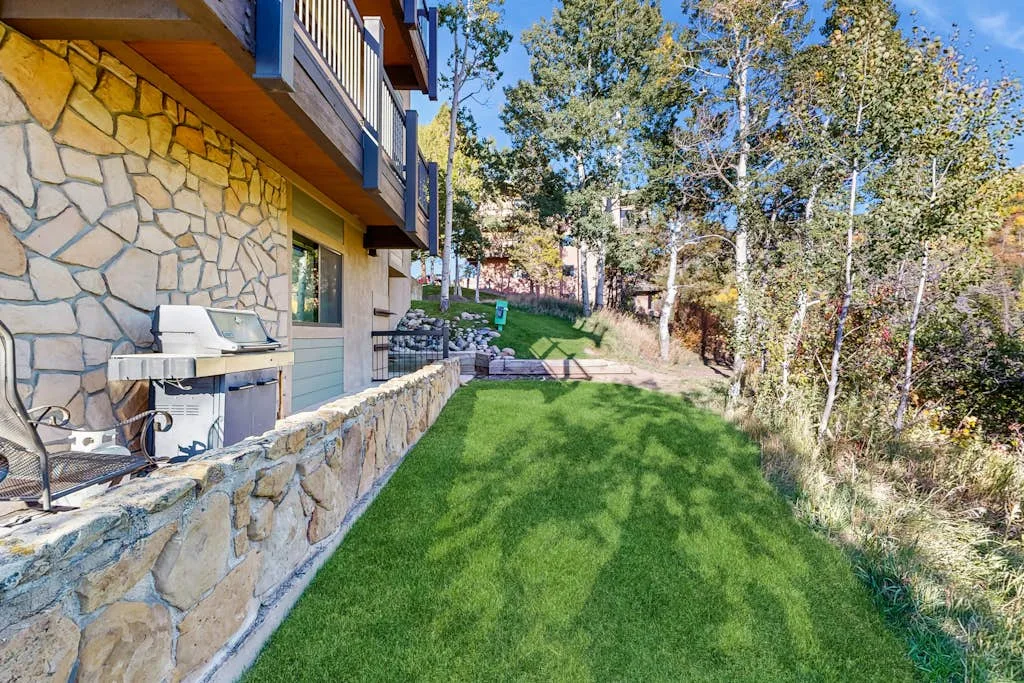 A grassy yard beside a stone-faced building, with outdoor seating and trees.