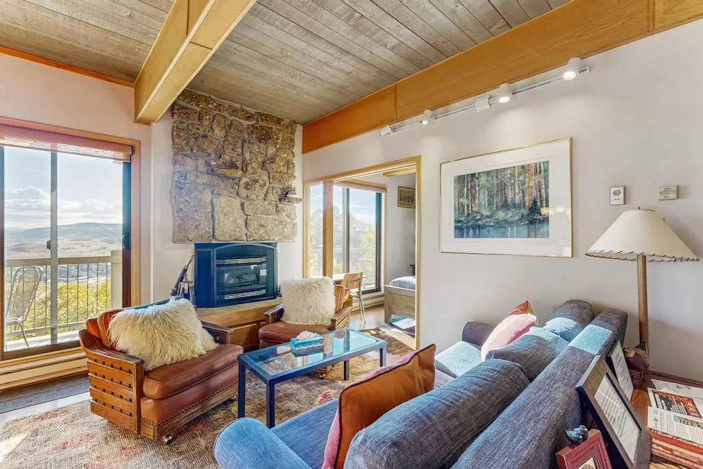 A living room with seating, a coffee table, and large windows overlooking the landscape.