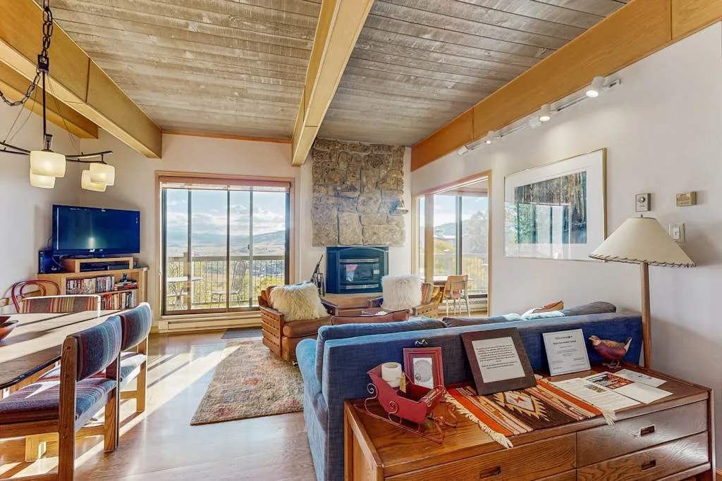 A living room with seating, a stone fireplace, and large windows.