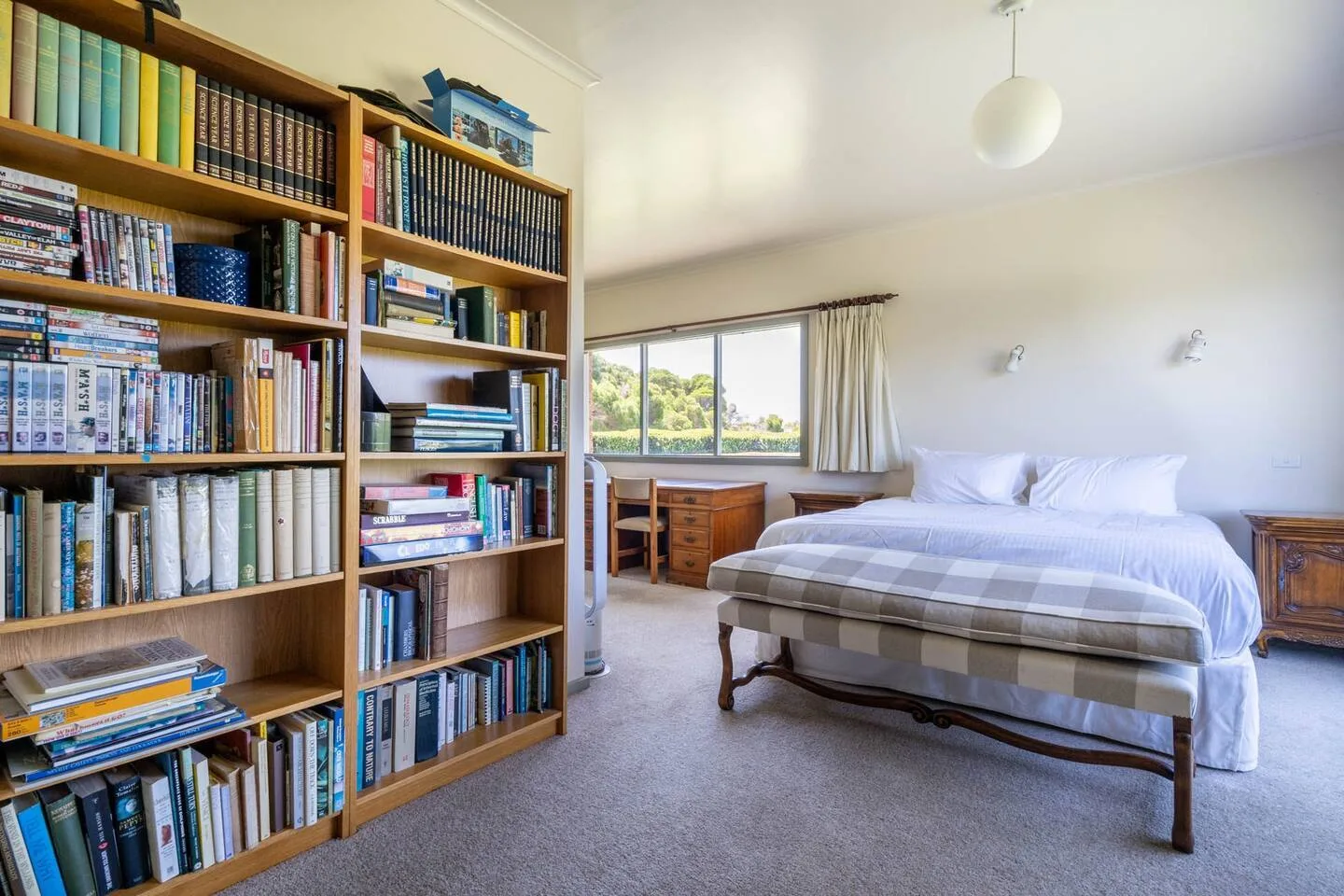 Dormitorio con una cama, estanterías llenas de libros y un escritorio junto a la ventana.