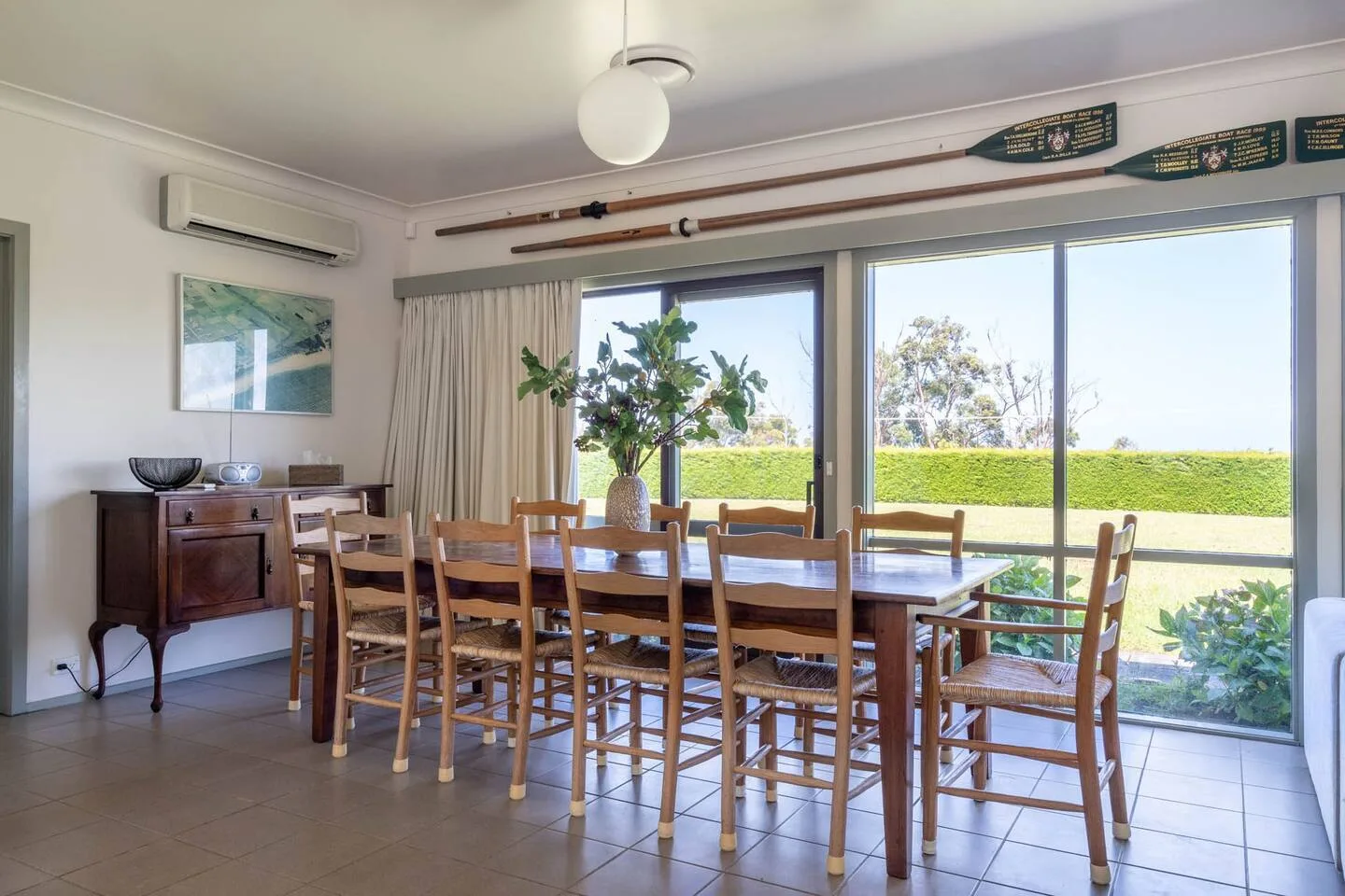 Una gran mesa de comedor ofrece vistas a una exuberante vegetación e invita a los huéspedes a reunirse para comer en casa.