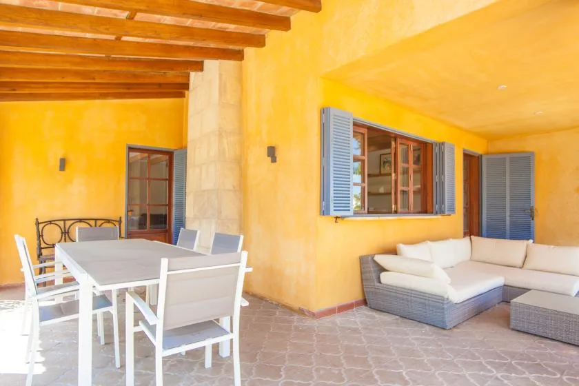A covered patio has a dining table and seating beside a window.