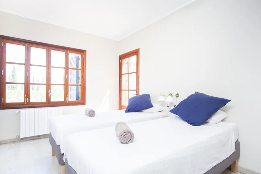A bright bedroom with two beds and large wood-framed windows.