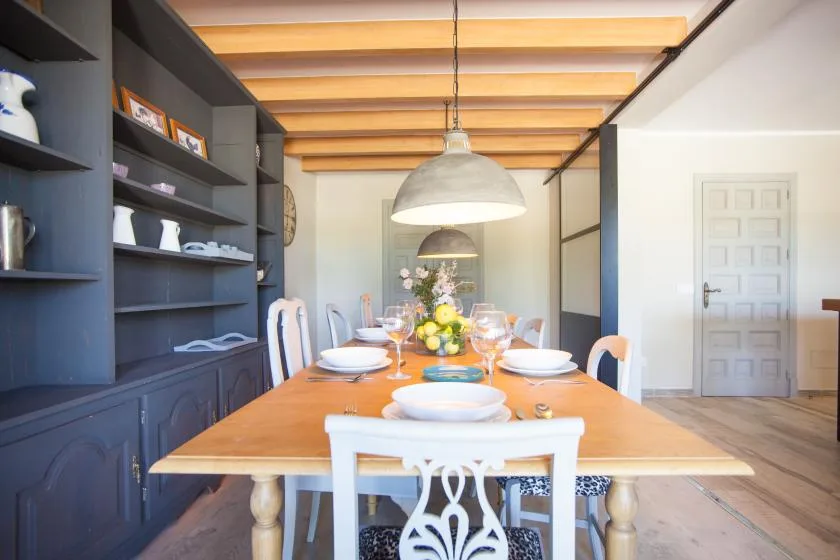 A dining room with a long set table beneath exposed ceiling beams.