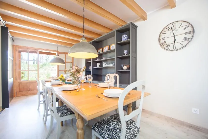 A bright dining room with a wooden table beneath exposed ceiling beams.
