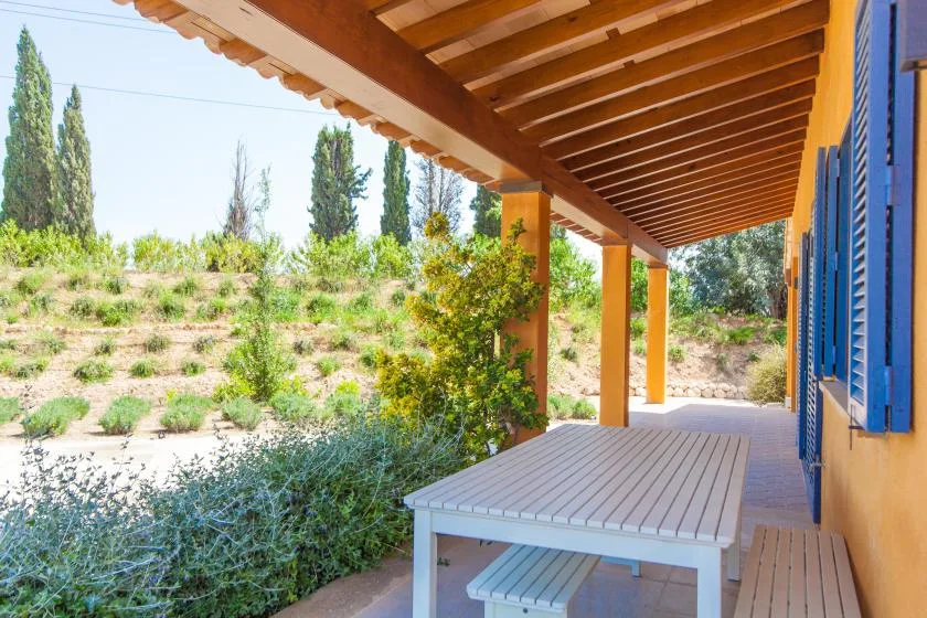 A covered porch with a white table overlooks a landscaped hillside.