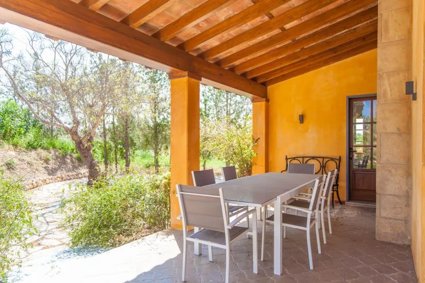 A covered patio with a dining table and chairs overlooks a garden.