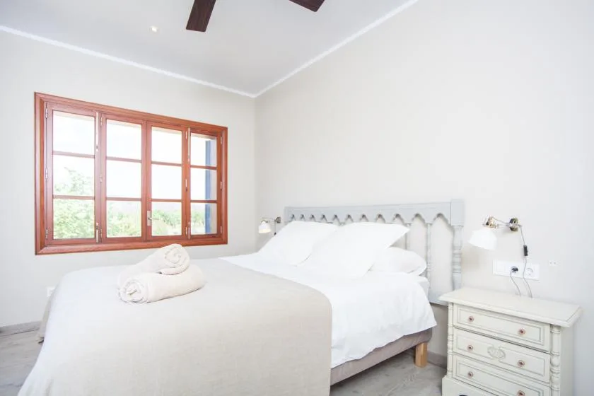 A bright bedroom with a bed beneath a wooden-framed window.