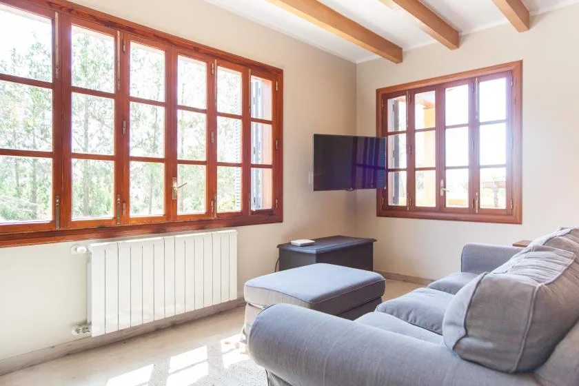 A bright living room with large wood-framed windows and gray seating.