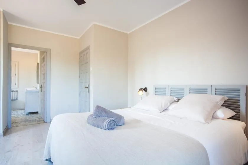 A bright bedroom with a neatly made bed and an open doorway.