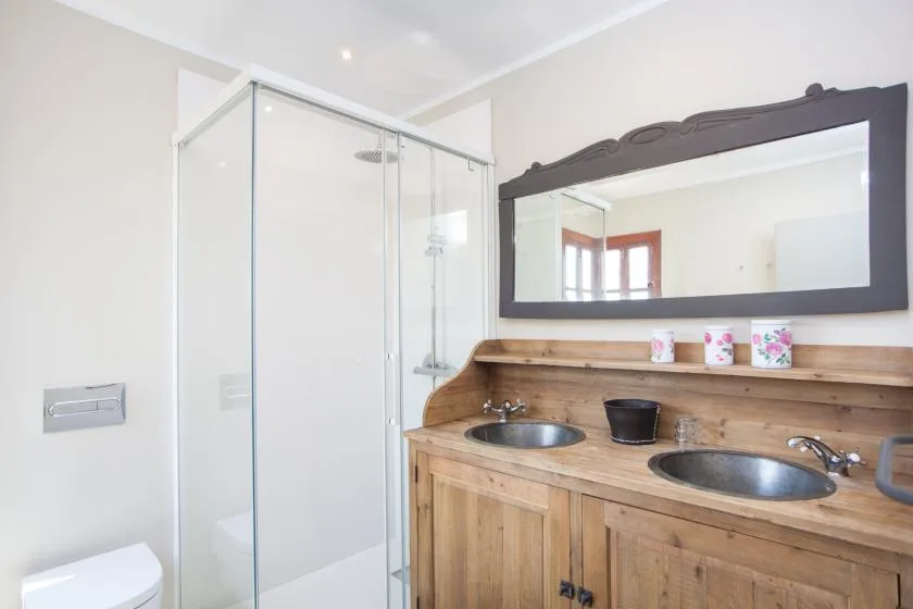 A bathroom with a glass shower and a wooden vanity beneath a large mirror.