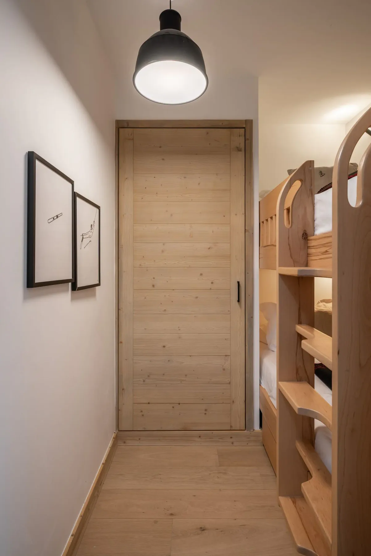 Narrow room with wooden bunk beds, a sliding wooden door, wall sconce lighting, and framed art on the wall.