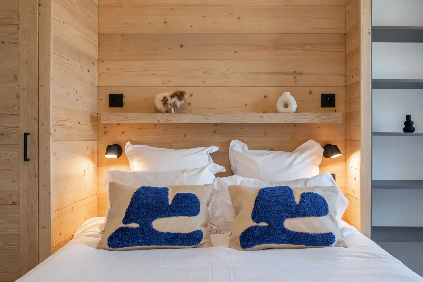 Cozy bedroom with a wooden accent wall, bed with decorative pillows, wall-mounted TV, and a view of mountains through the window.