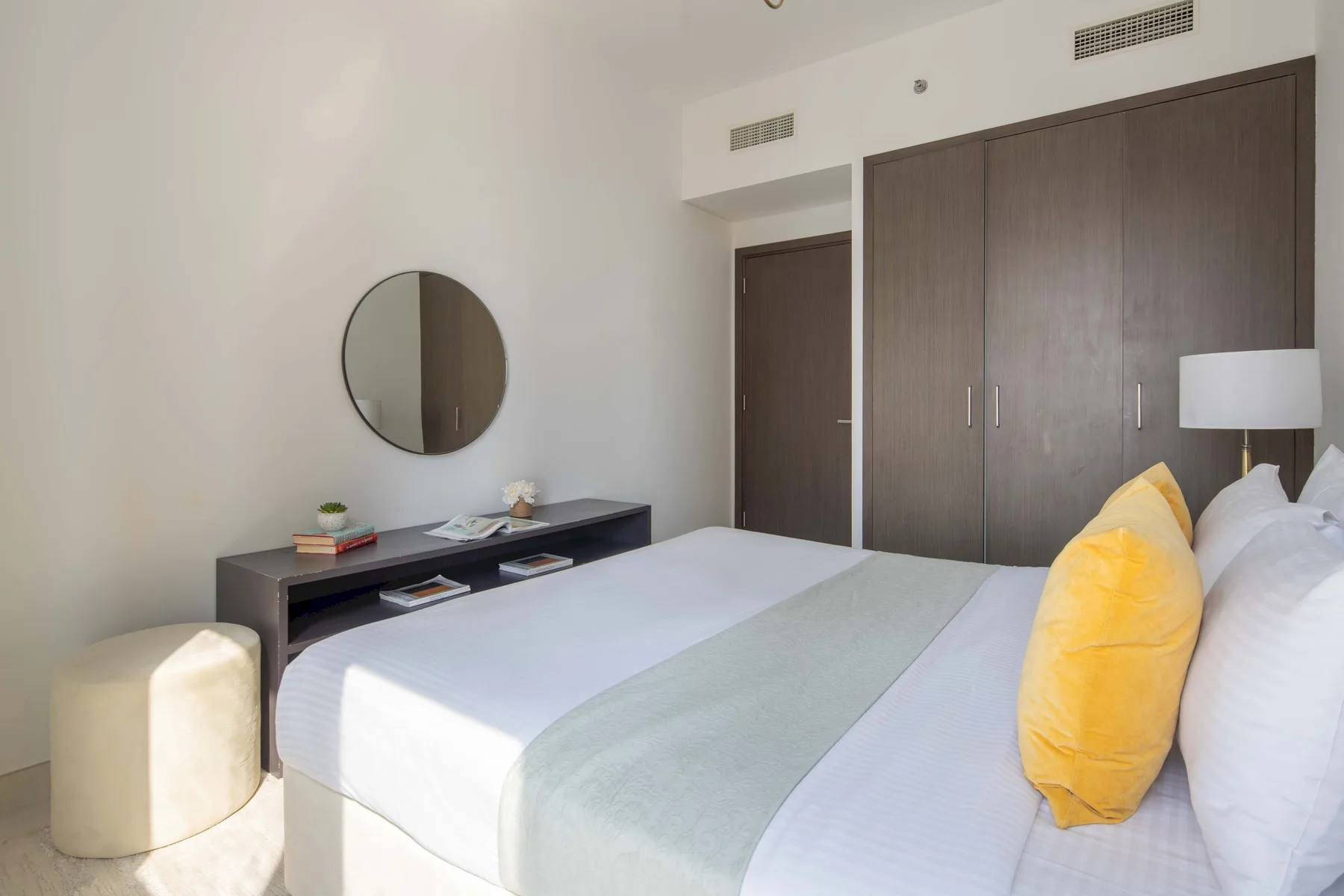 Dormitorio con una cama bien tendida, un cojín amarillo y un armario oscuro.