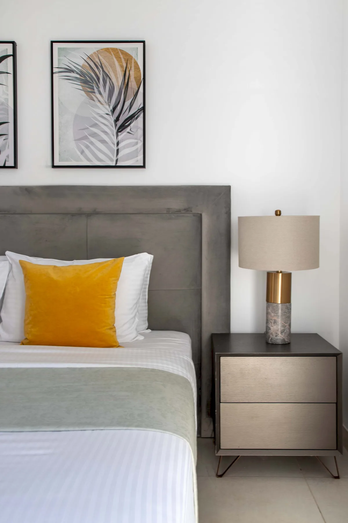 Un dormitorio con una cama bien tendida, un cojín mostaza y una mesita de noche.