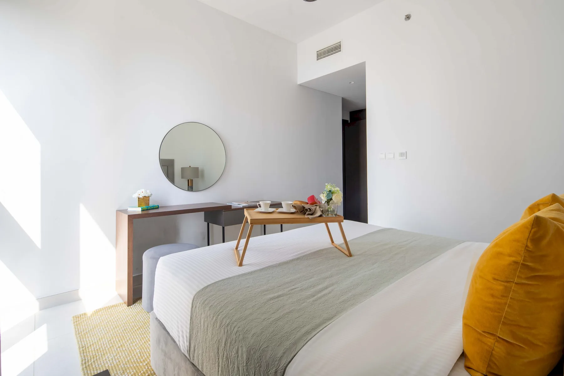 Un dormitorio con una cama bien arreglada, una mesa auxiliar y un espejo redondo en la pared.