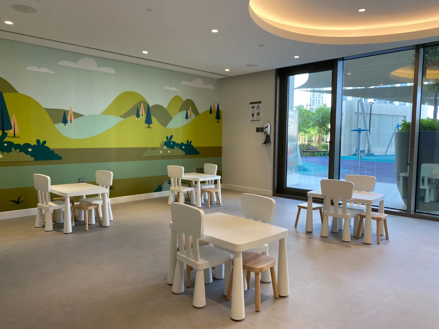Un comedor interior luminoso con mesas pequeñas y asientos junto a grandes ventanales.