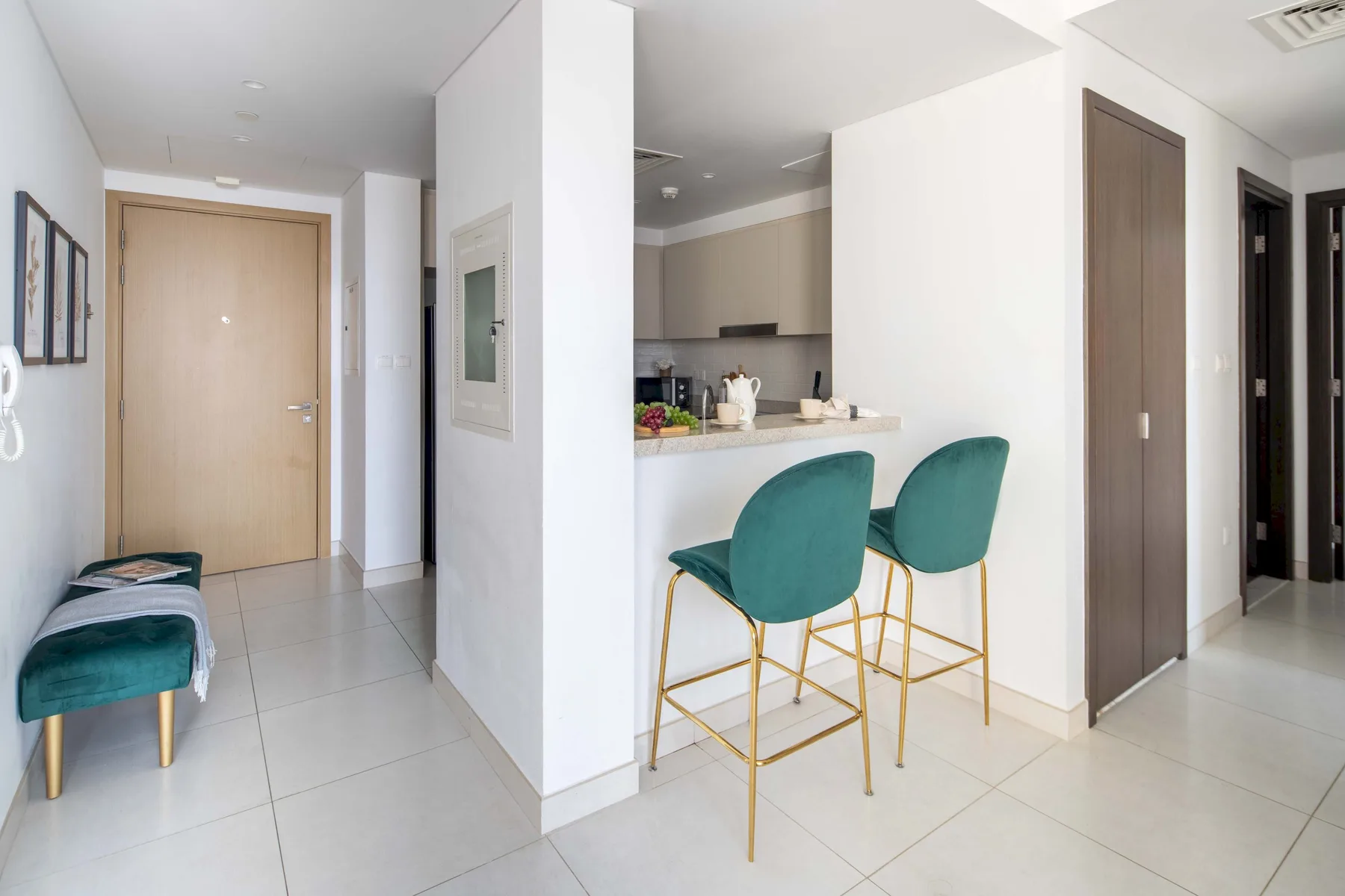 Una entrada luminosa se abre a una cocina compacta con una barra y asientos verde azulado.