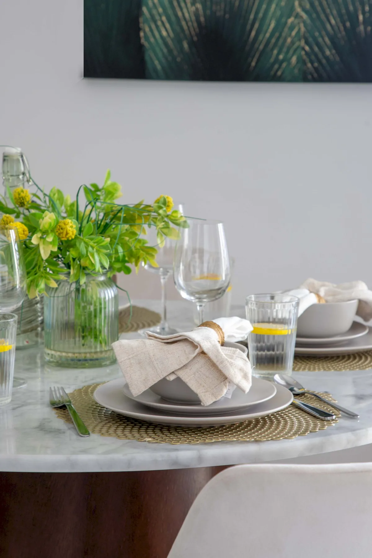 Una mesa de comedor está preparada con platos, copas, servilletas dobladas y un arreglo floral.