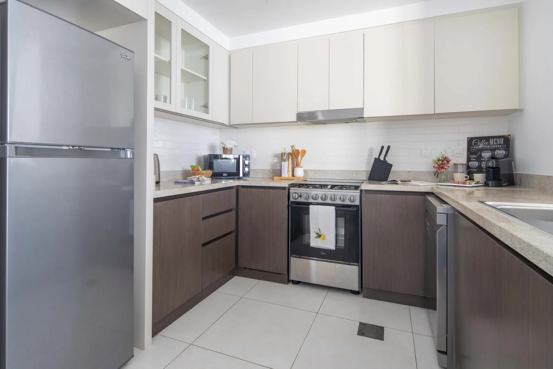 Una cocina luminosa con encimeras en L, armarios y electrodomésticos de acero inoxidable.