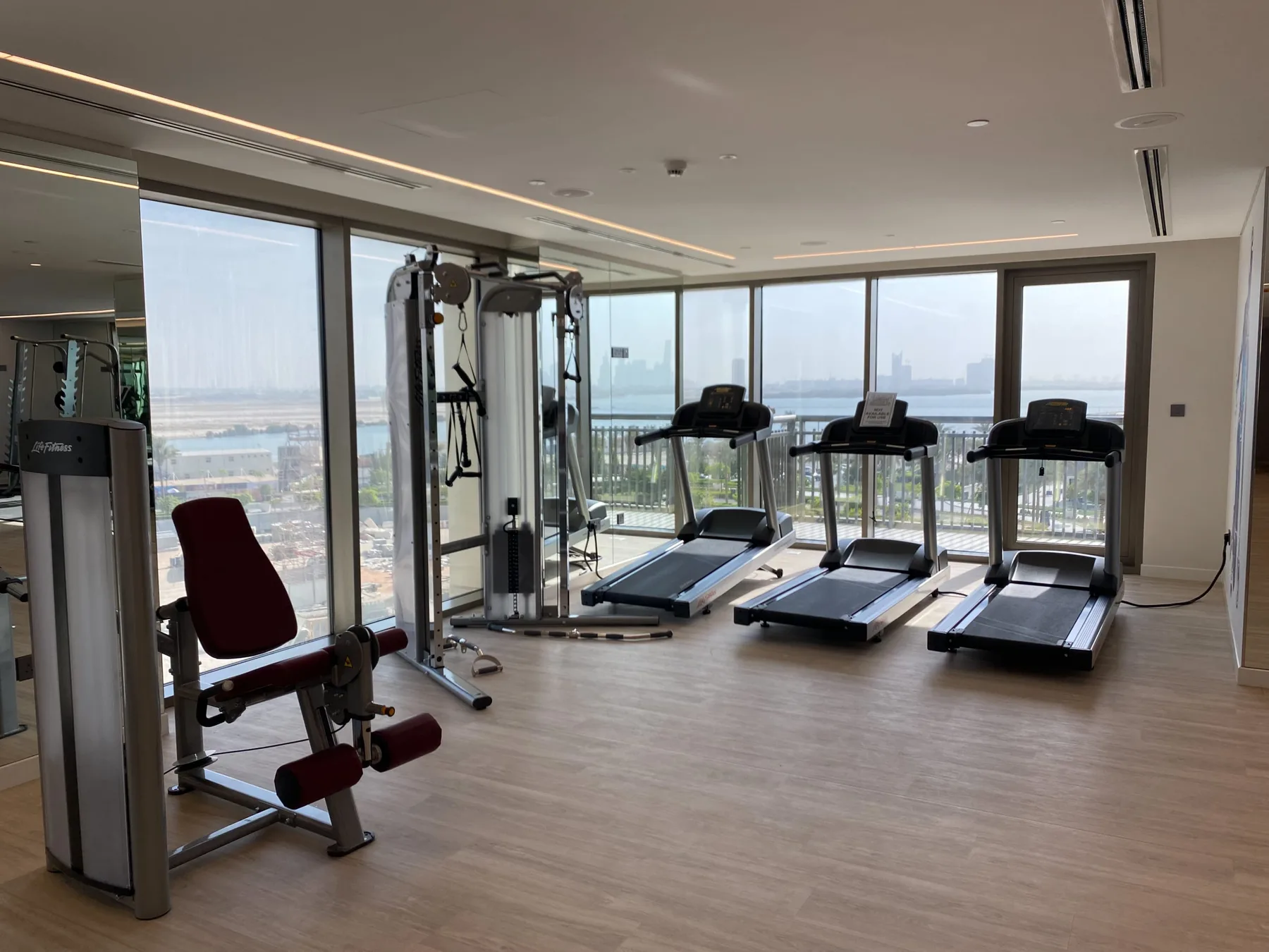 Una sala de ejercicio con cintas de correr y equipos junto a ventanales.