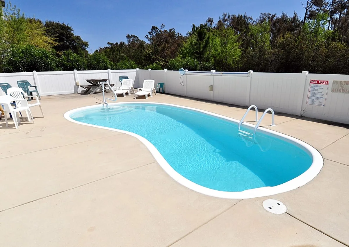An outdoor swimming pool with seating on a paved deck.