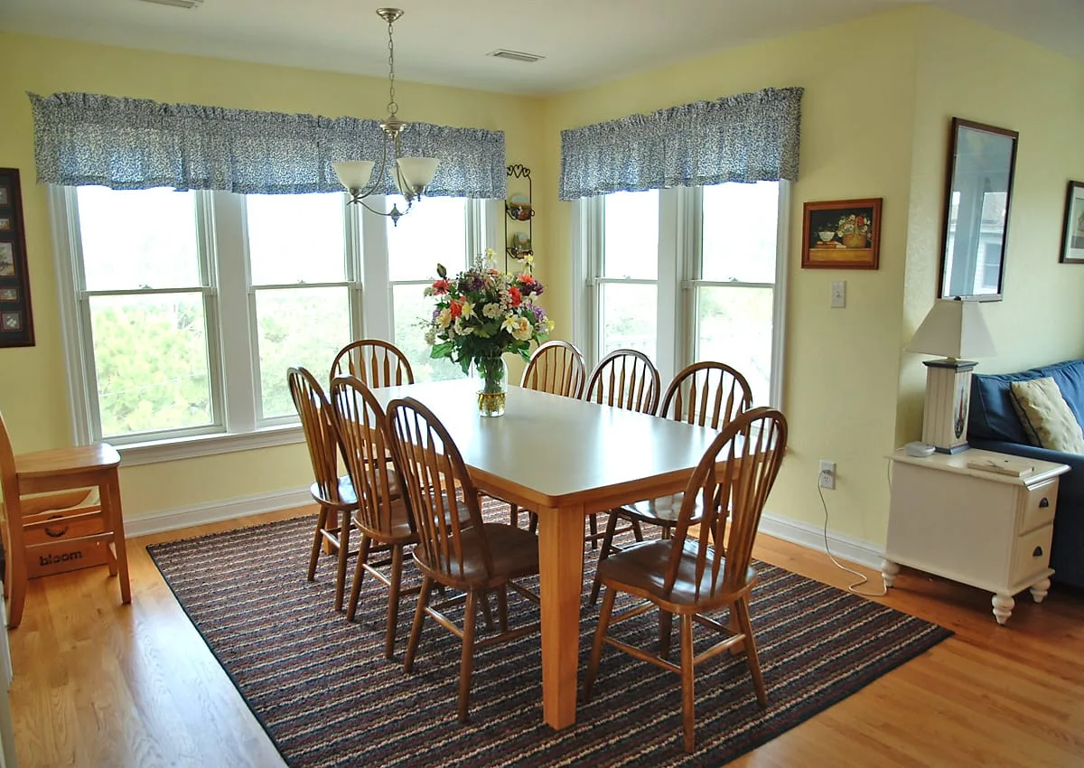 A dining room with a wooden table and chairs beside several windows.