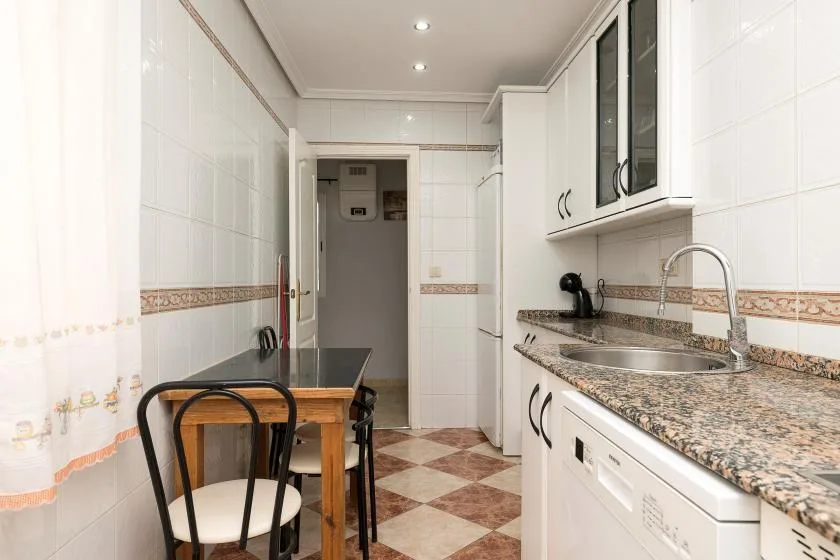 A tiled kitchen with a long counter, sink, and small dining table.