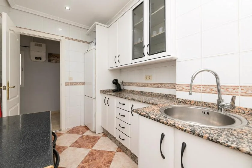 A tiled kitchen with white cabinets and a long countertop.