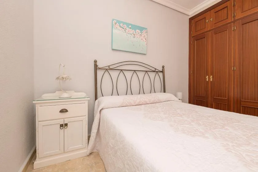 A bedroom with a bed, a bedside cabinet, and built-in wooden wardrobes.