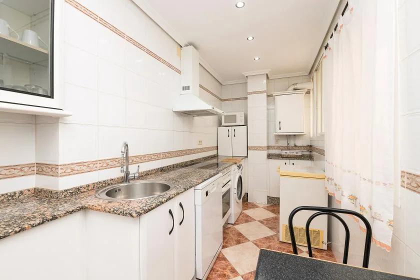 A narrow kitchen with white cabinets, a countertop, and a sink.