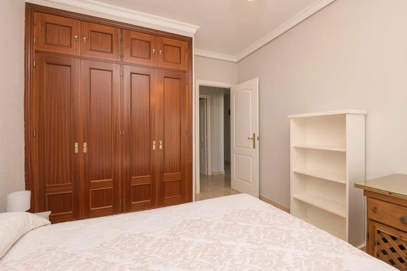 A bedroom with a bed, wooden wardrobe, and open shelving.
