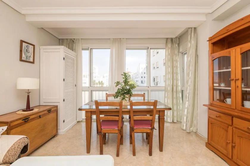 A dining area with a wooden table and chairs beside large windows.