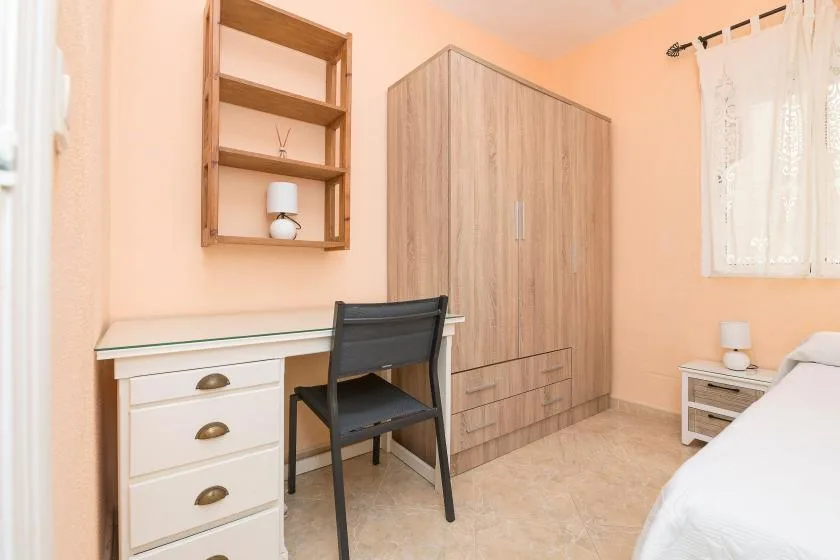 A bedroom with a desk and chair beside a wooden wardrobe.
