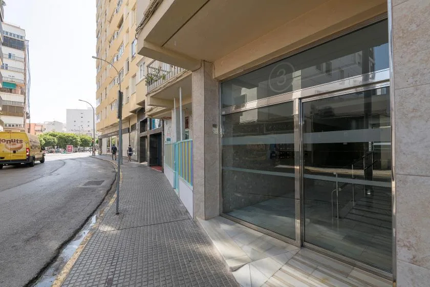 A city sidewalk runs past a building entrance with large glass doors.
